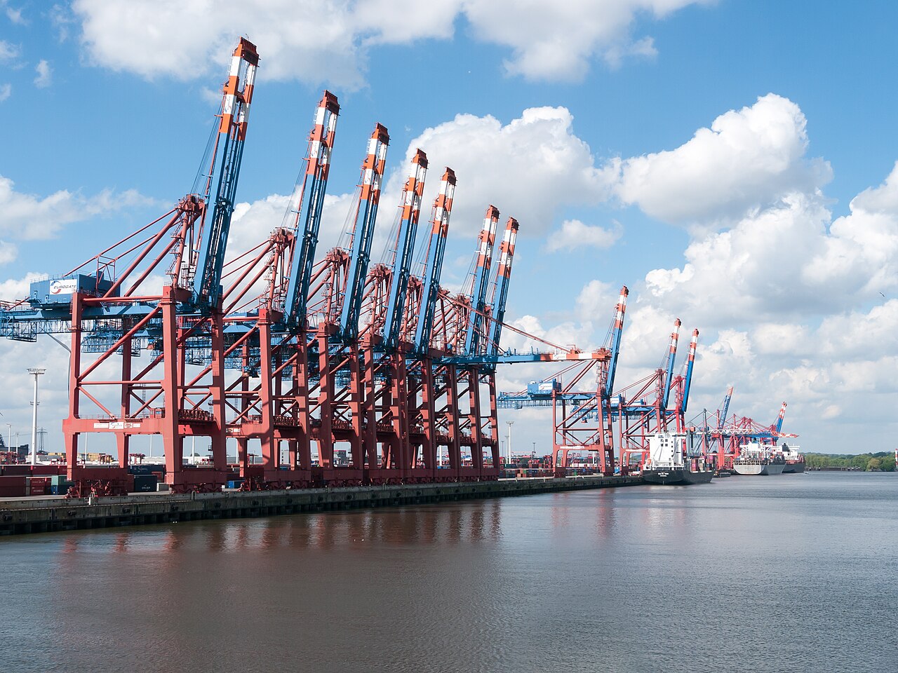 Red and blue container cranes beside cargo ships at Hamburg’s EUROGATE terminal.
